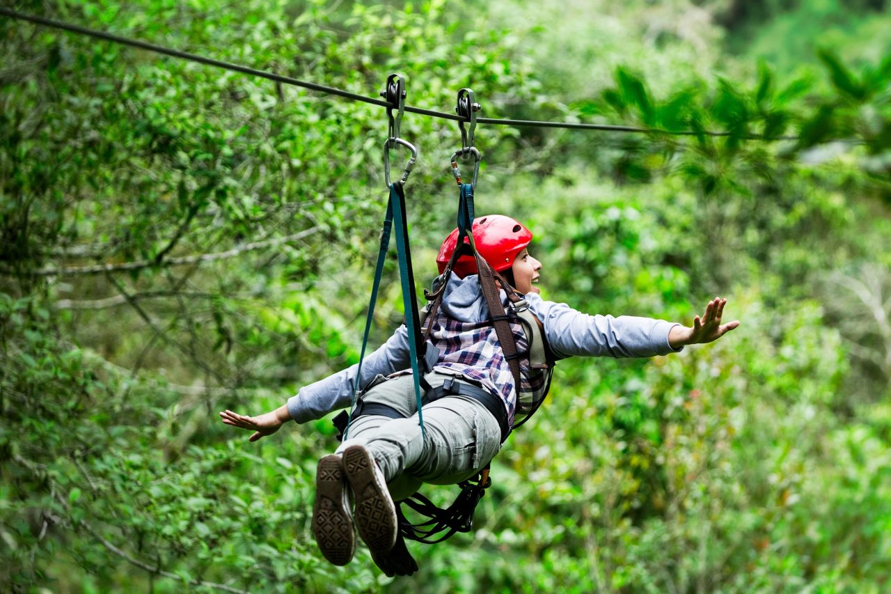 Adult tourist wearing casul clothing on zip line trip, selective focus against blured forest